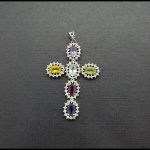Cruz de oro blanco con circonitas de varios colores y rodeada de circonitas blancas