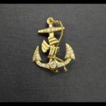 Broche oro amarillo 18k con forma de ancla decorado con puntas de brillantes y en el centor un brillante de 0,15qtes