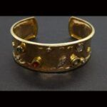 Pulsera oro amarillo 18k rigida abierta con textura, decorada con puntas de brillantes y piedras de color azul, corinto y verde