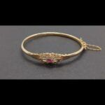 Pulsera ovalada oro amarillo 18k parte central con un rubí y circonitas blancas, cierre con cadena de seguridad